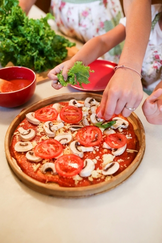 child hand helping put topping on a pizza