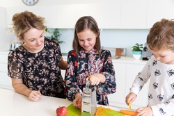 Mother and two children in kitchen, grating and chopping carrots 