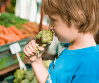 Little boy smelling a artichoke in a grocery store